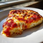 A close-up slice of pizza showing a thick, sturdy cauliflower pizza crust topped with melted cheese and tomato sauce.