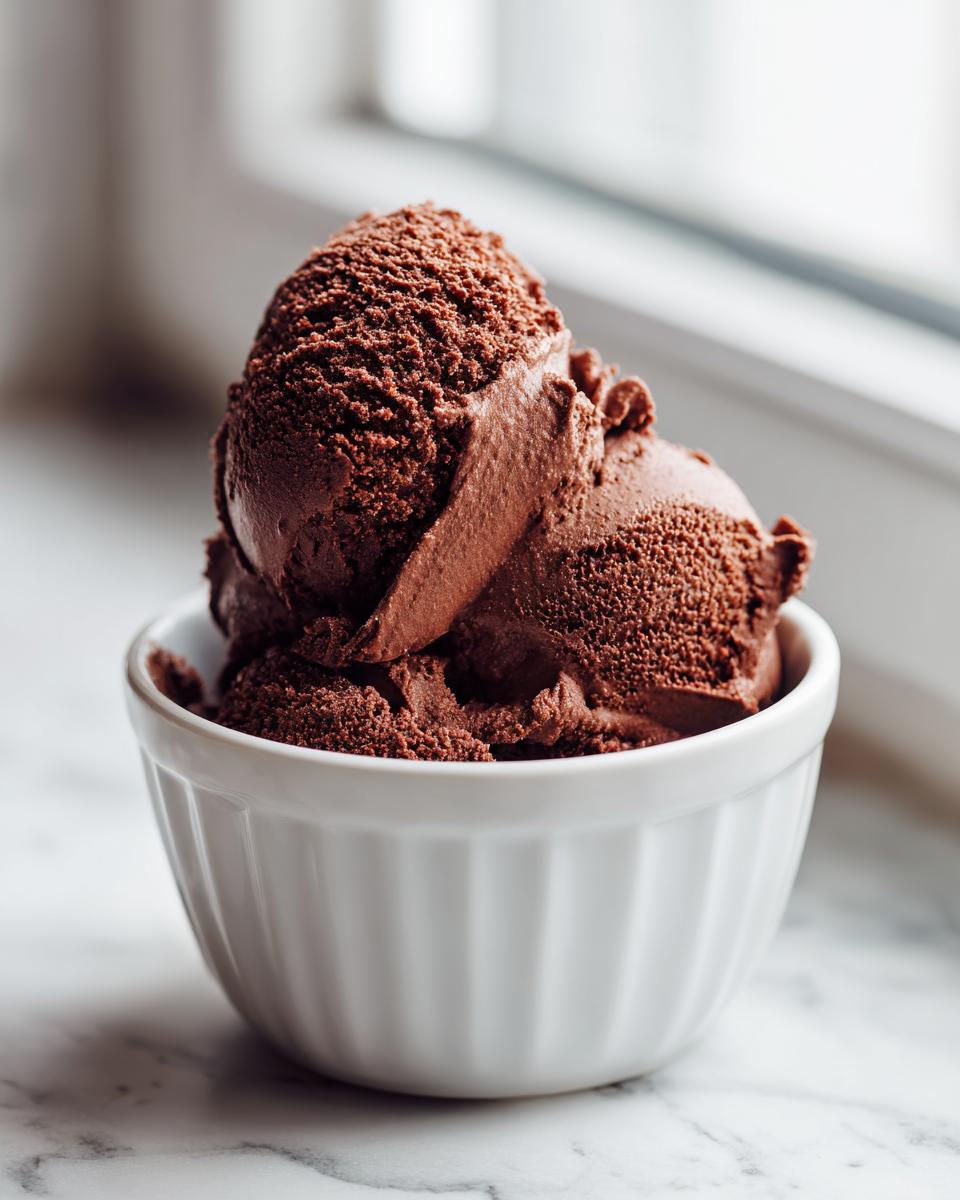 Three scoops of rich, dark chocolate mousse served in a white fluted ramekin, resembling ice cream texture.