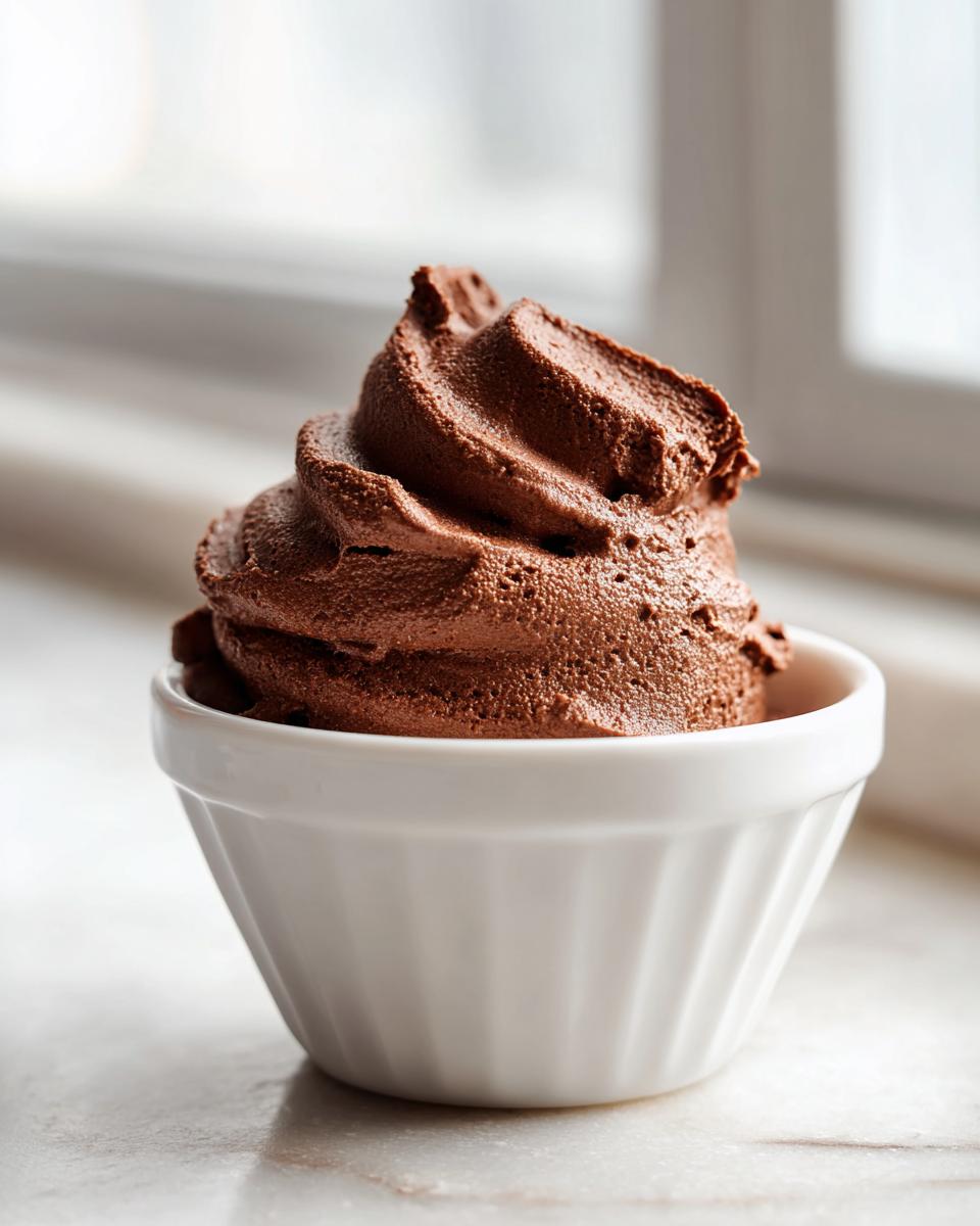 A decadent swirl of rich chocolate mousse served in a small white ramekin, set against a bright window background.