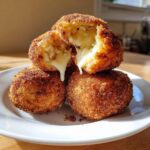 Close-up of crispy, golden air fryer arancini stacked, with one broken open showing melted cheese stretching out.