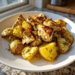 Close-up of seasoned, browned pieces of air fryer greek chicken with potatoes on a white plate.