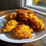 A pile of golden brown, crispy air fryer onion pakora served on a white plate near a sunlit window.