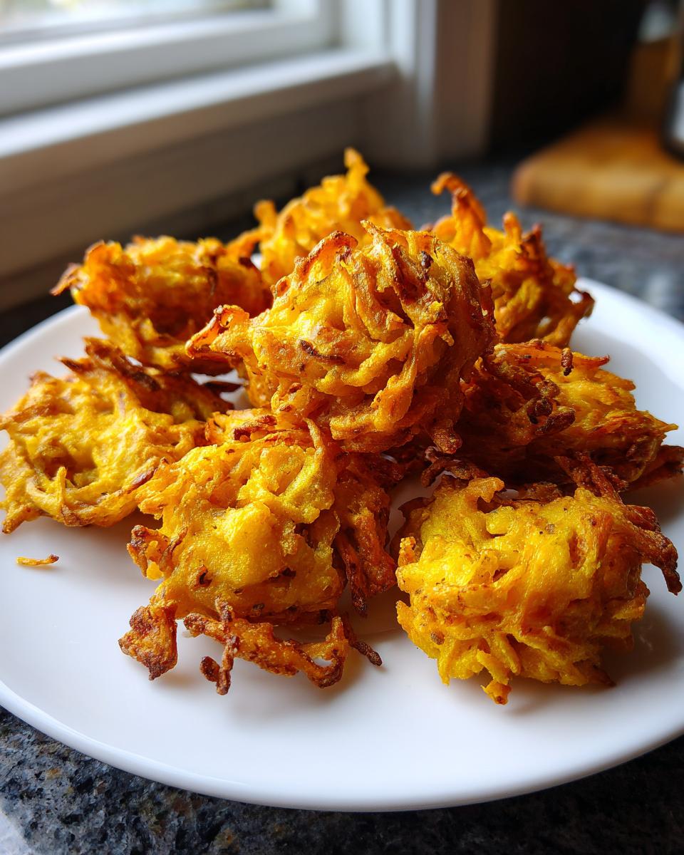 A close-up of several golden-brown, crispy air fryer onion pakora stacked on a white plate.
