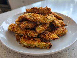 A mound of golden brown, crispy air fryer pickle fries stacked high on a white plate.