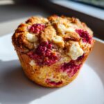Close-up of a perfectly baked air fryer raspberry and white chocolate muffin with visible fruit and melted chocolate chunks.