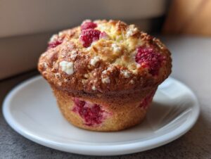 Close-up of a golden-brown air fryer raspberry and white chocolate muffin with visible raspberries and crumb topping.