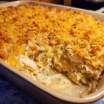 A scoop has been taken from a creamy chicken noodle casserole topped with golden crushed crackers and melted cheese.