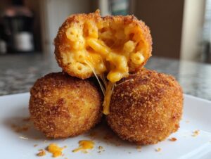 Close-up of three golden brown fried mac and cheese balls, one cut open showing melted cheese stretching.