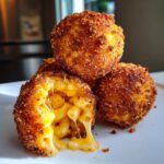 Close-up of golden brown fried mac and cheese balls, one cut open showing melted cheese and macaroni noodles.