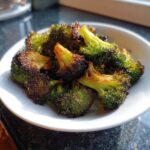 Close-up of perfectly crispy roasted broccoli florets with caramelized, slightly charred edges served in a white bowl.