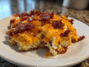 A close-up of a serving of bacon cheeseburger casserole topped with melted cheddar and crispy bacon pieces.