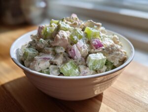 A close-up of creamy, chunky chicken salad featuring diced chicken, celery, and red onion in a white bowl.