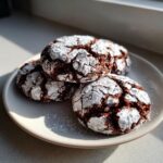 A stack of four rich, dark brown butter toffee chocolate crinkle cookies heavily dusted with powdered sugar.