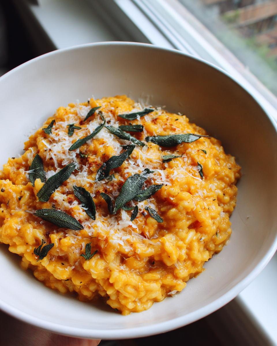 Close-up of creamy butternut squash risotto topped with grated Parmesan cheese and crispy fried sage leaves.