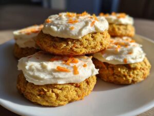 A close-up stack of delicious carrot cake cookies topped with thick cream cheese frosting and shredded carrots.