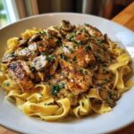 A white bowl filled with fettuccine pasta topped with seared chicken pieces and mushrooms in a rich, creamy sauce, garnished with parsley, representing chicken marsala pasta.