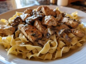 A close-up serving of creamy chicken marsala pasta featuring browned chicken pieces and sliced mushrooms over wide egg noodles.