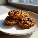 A stack of three golden, textured breakfast cookie treats loaded with visible chocolate chips, resting on a white plate.