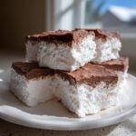 Four squares of fluffy white Cool Whip candy topped with rich chocolate frosting stacked on a white plate.