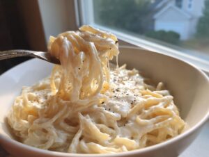 A fork lifts a generous portion of creamy cottage cheese pasta from a white bowl, seasoned with black pepper.