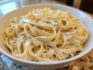 Close-up of creamy fettuccine pasta coated in a rich white sauce, served in a white bowl.