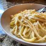 Close-up of creamy fettuccine pasta coated in a rich white sauce and black pepper, served in a white bowl.
