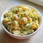 A close-up of creamy pickle pasta salad in a white bowl, garnished generously with fresh dill.