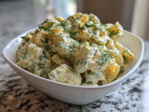 A close-up of creamy pickle pasta salad topped generously with fresh dill, served in a white bowl.