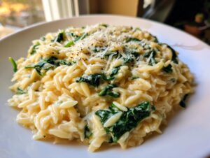 Close-up of creamy spinach orzo pasta topped with grated Parmesan cheese and black pepper.