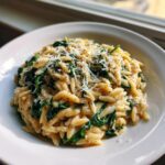 A close-up of creamy orzo pasta mixed with wilted spinach and topped with grated Parmesan cheese.
