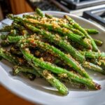 Close-up of bright green beans coated in crispy Parmesan breading, served on a white dish.