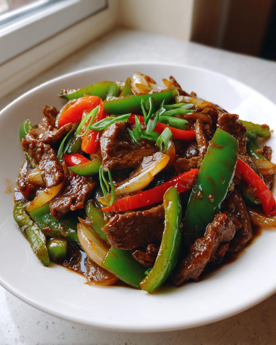 Close-up of a rich, saucy pepper steak dish featuring strips of beef, green and red bell peppers, and onions, garnished with scallions.