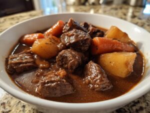 Close-up of a white bowl filled with rich, dark brown beef stew featuring tender chunks of beef, carrots, and potatoes.