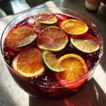 Close-up overhead view of a bowl of vibrant red firecracker punch garnished with floating slices of orange and lime.