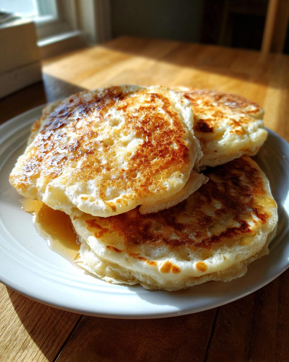 A stack of three fluffy buttermilk pancakes drizzled with syrup, sitting on a white plate.