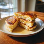 A stack of three fluffy buttermilk pancakes, cut to show the airy interior, drizzled with syrup.