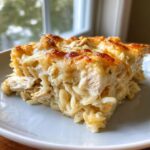 A close-up of a hearty slice of french onion chicken orzo casserole with a golden, bubbly cheese topping.