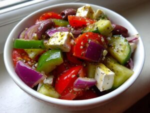 A close-up view of a vibrant greek salad featuring chunks of feta, tomatoes, cucumbers, red onion, and olives dressed with herbs.