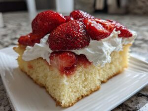 Close-up of a moist slice of german strawberry cake topped with fresh strawberries and whipped cream on a white plate.