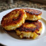 Three perfectly pan-fried mashed potato cakes with a crispy, golden-brown exterior stacked on a white plate.