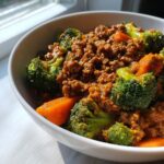 A close-up of a white bowl filled with savory ground beef stir fry mixed with bright green broccoli florets and orange carrots.