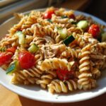 A close-up serving of healthy chicken pasta salad featuring rotini pasta, shredded chicken, cherry tomatoes, and cucumber chunks.