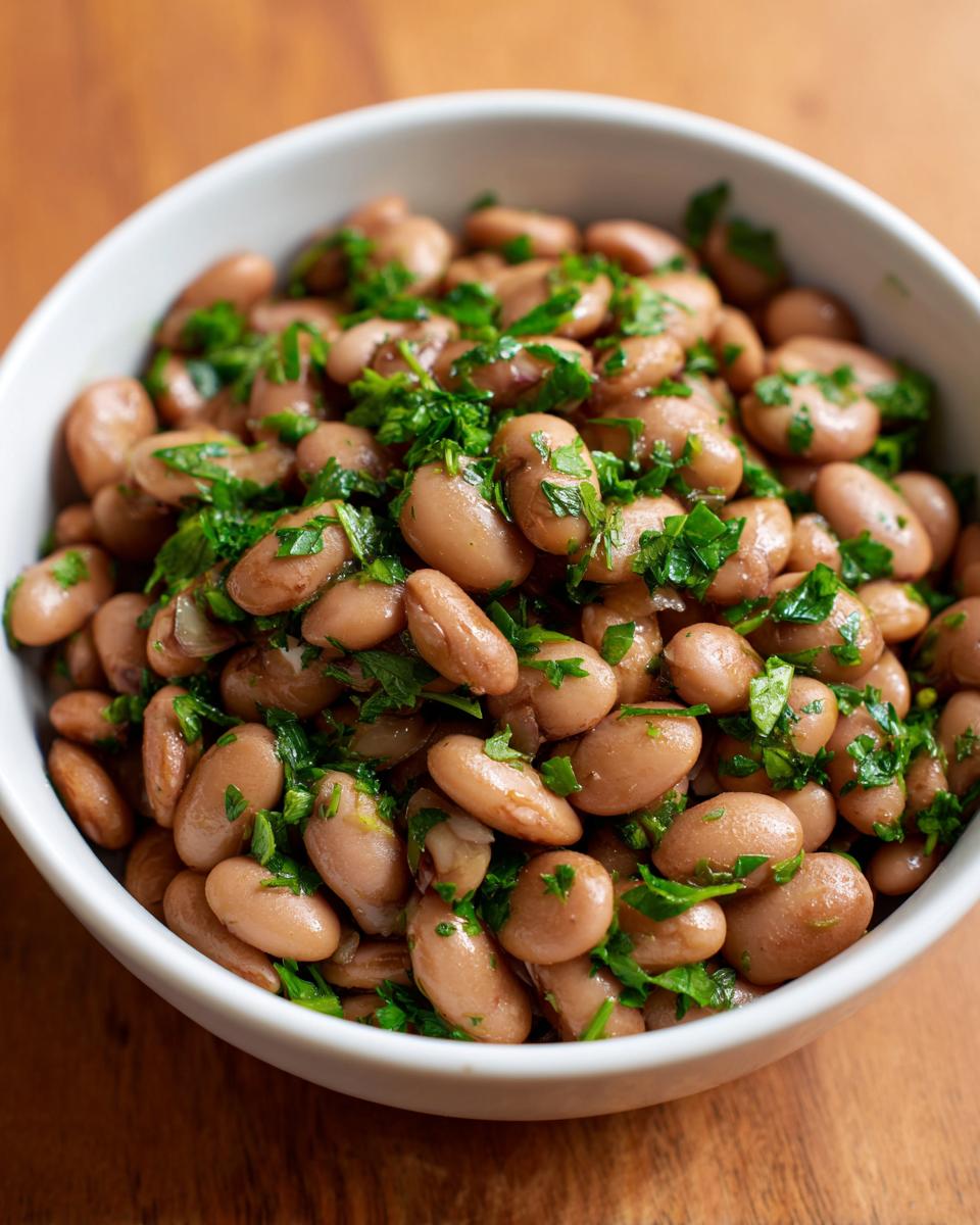 Close-up of a white bowl filled with cooked healthy pinto beans seasoned with fresh chopped parsley.