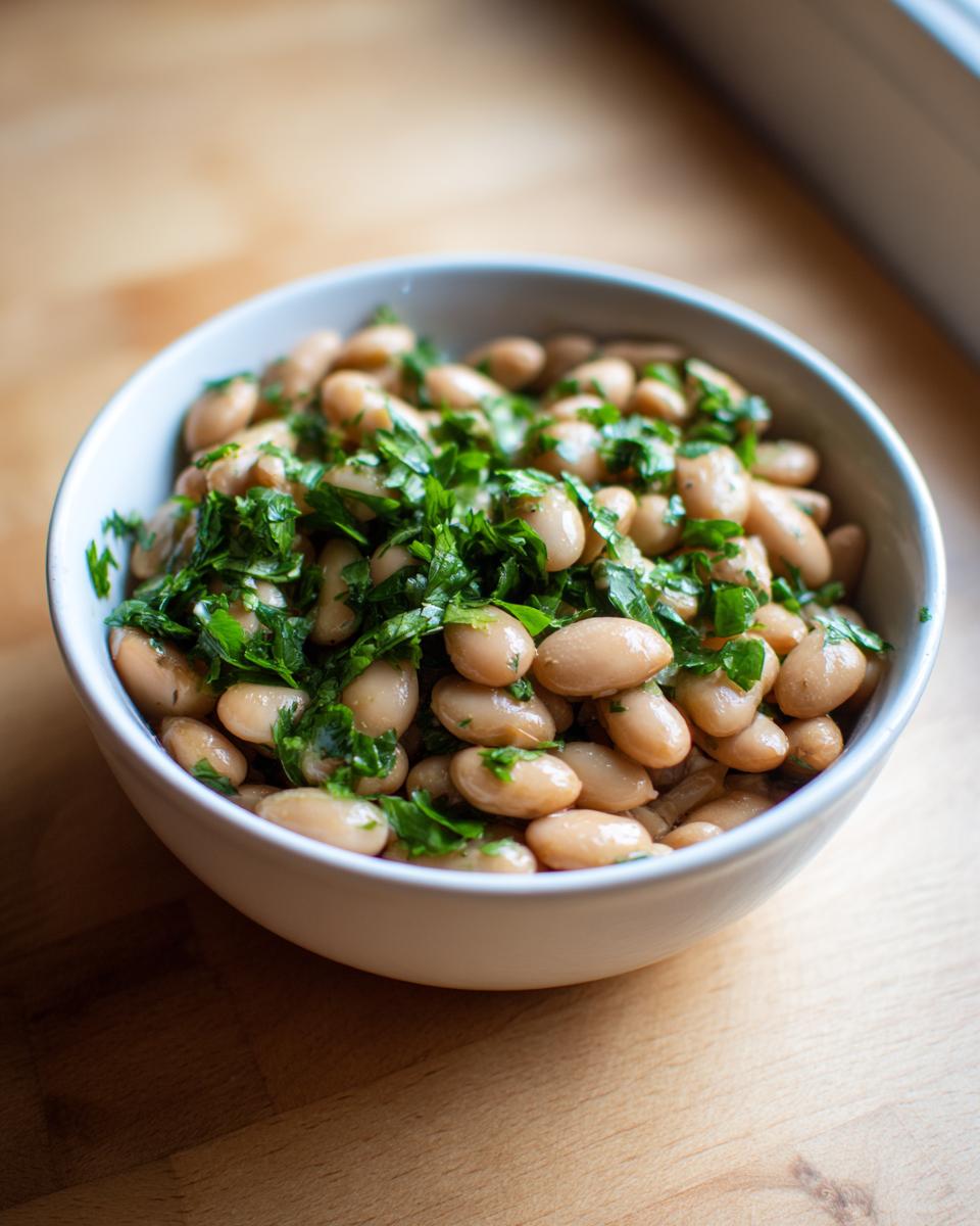 A white bowl filled with cooked, creamy healthy pinto beans garnished generously with fresh chopped parsley.