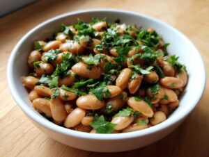 Close-up of a white bowl filled with seasoned, light brown healthy pinto beans topped generously with chopped fresh parsley.