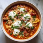 Overhead view of a hearty bowl of lasagna soup topped with dollops of ricotta, grated cheese, and fresh basil.
