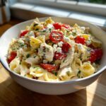 Close-up of a white bowl filled with high protein greek pasta salad featuring bowtie pasta, chicken chunks, cherry tomatoes, and feta cheese.
