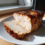 A thick slice cut from a seasoned, baked high-protein low-calorie chicken breast loaf on a white plate.