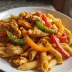 A close-up serving of Jamaican Rasta Pasta featuring penne, seasoned chicken, and vibrant slices of red, green, and yellow bell peppers.