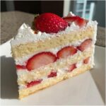 A perfect slice of japanese strawberry shortcake showing layers of fluffy sponge cake, whipped cream, and fresh strawberry slices.